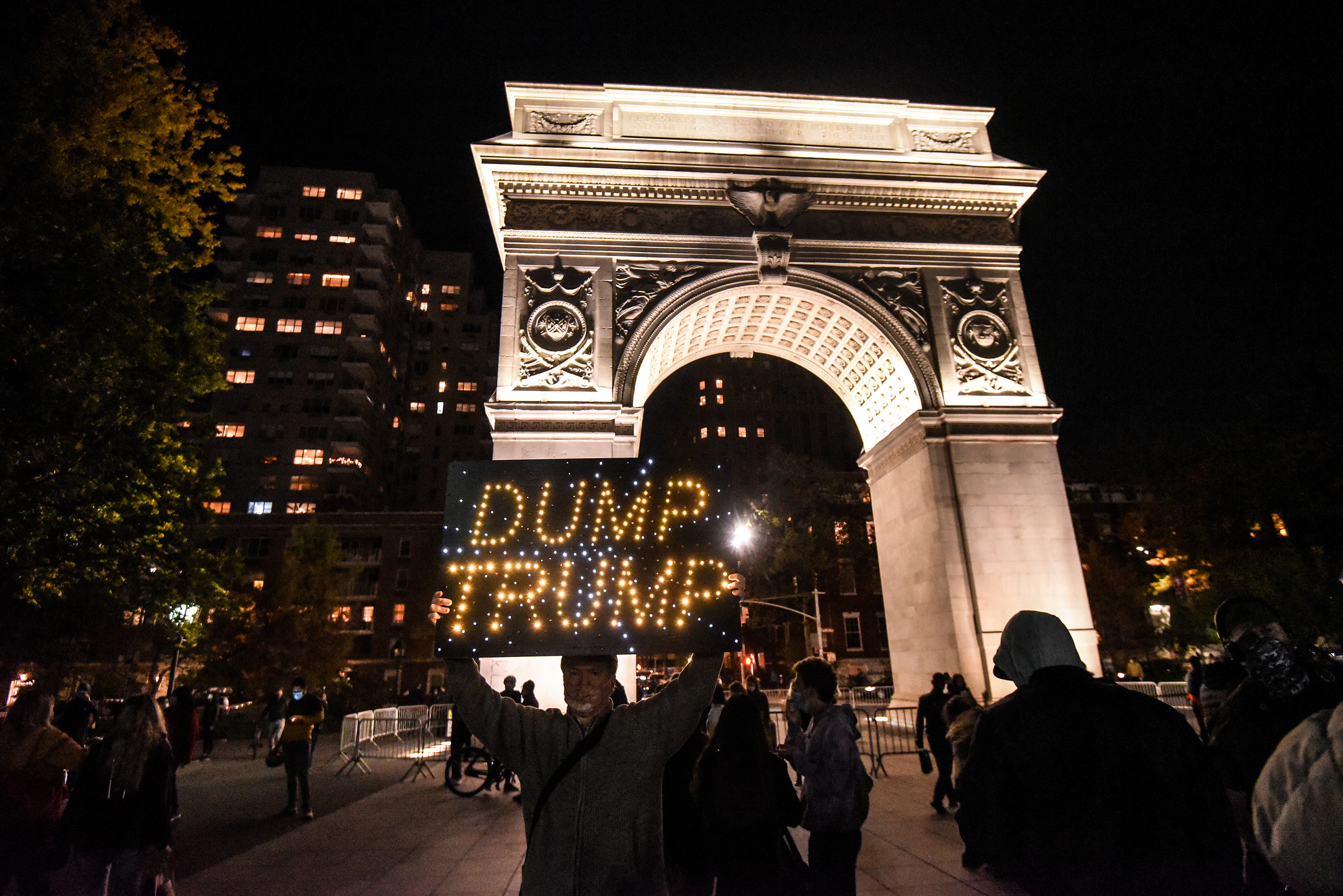 People dance to music during a anti-Trump pro-Biden rally in Washington Square Park in New York, New York, U.S. October 25, 2020. A person from an artist group called the Light Brigade holds a lighted sign saying "Dump Trump".